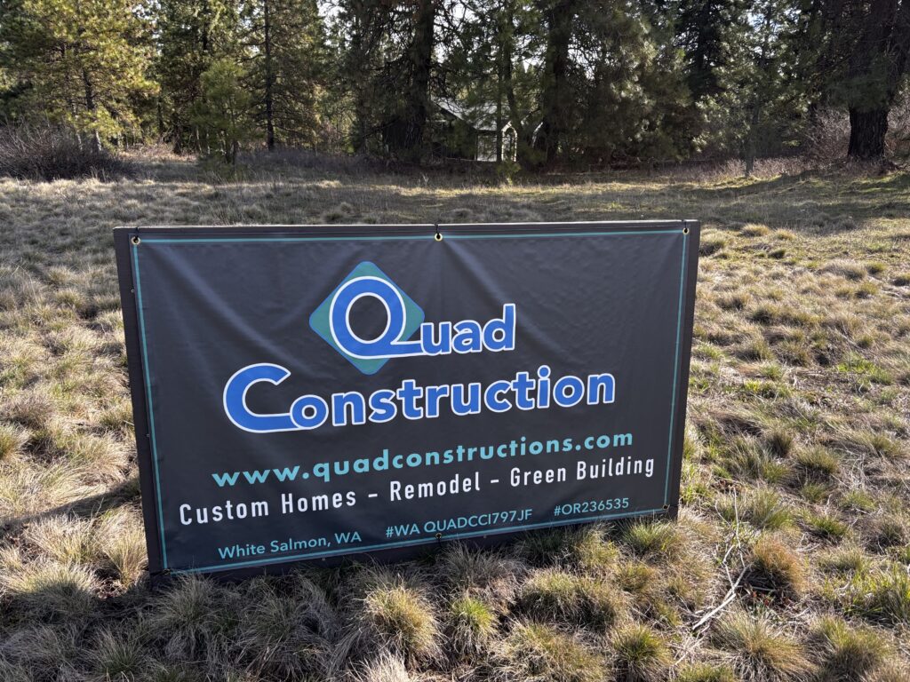 A Quad Construction sign sits on a grassy field with trees in the far distance.